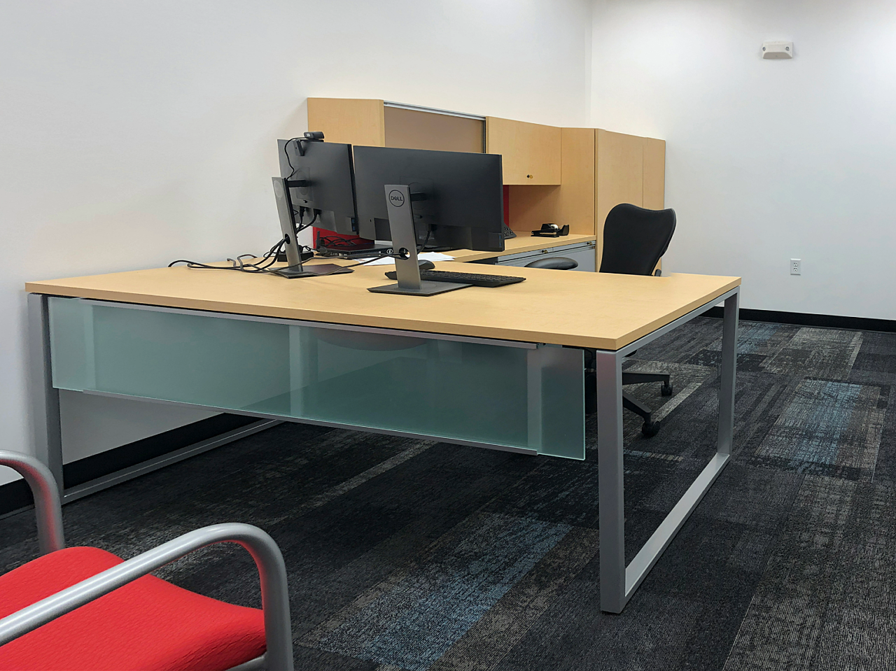 A modern private office with L-shaped desk, matching cabinets, dual monitors, and ergonomic chair for increased productivity.