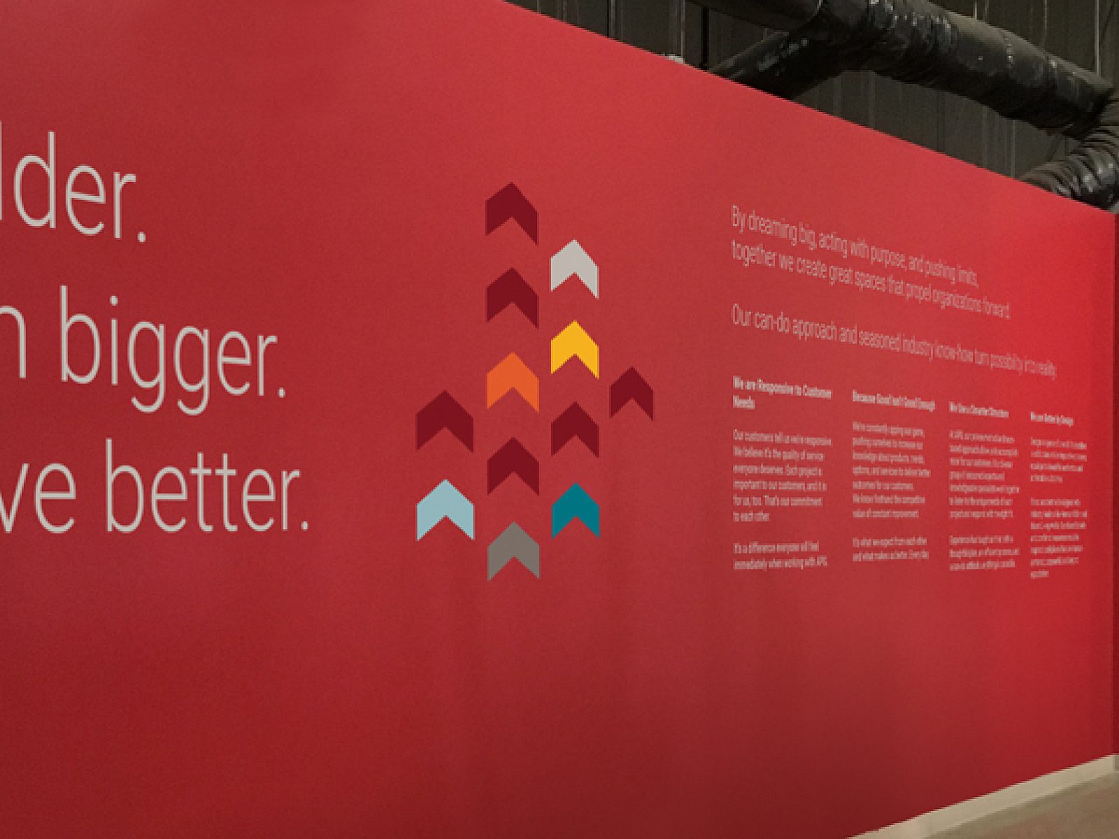 Red-painted wall in a tidy warehouse with inspirational brand message: Be bolder, dream bigger, achieve better.