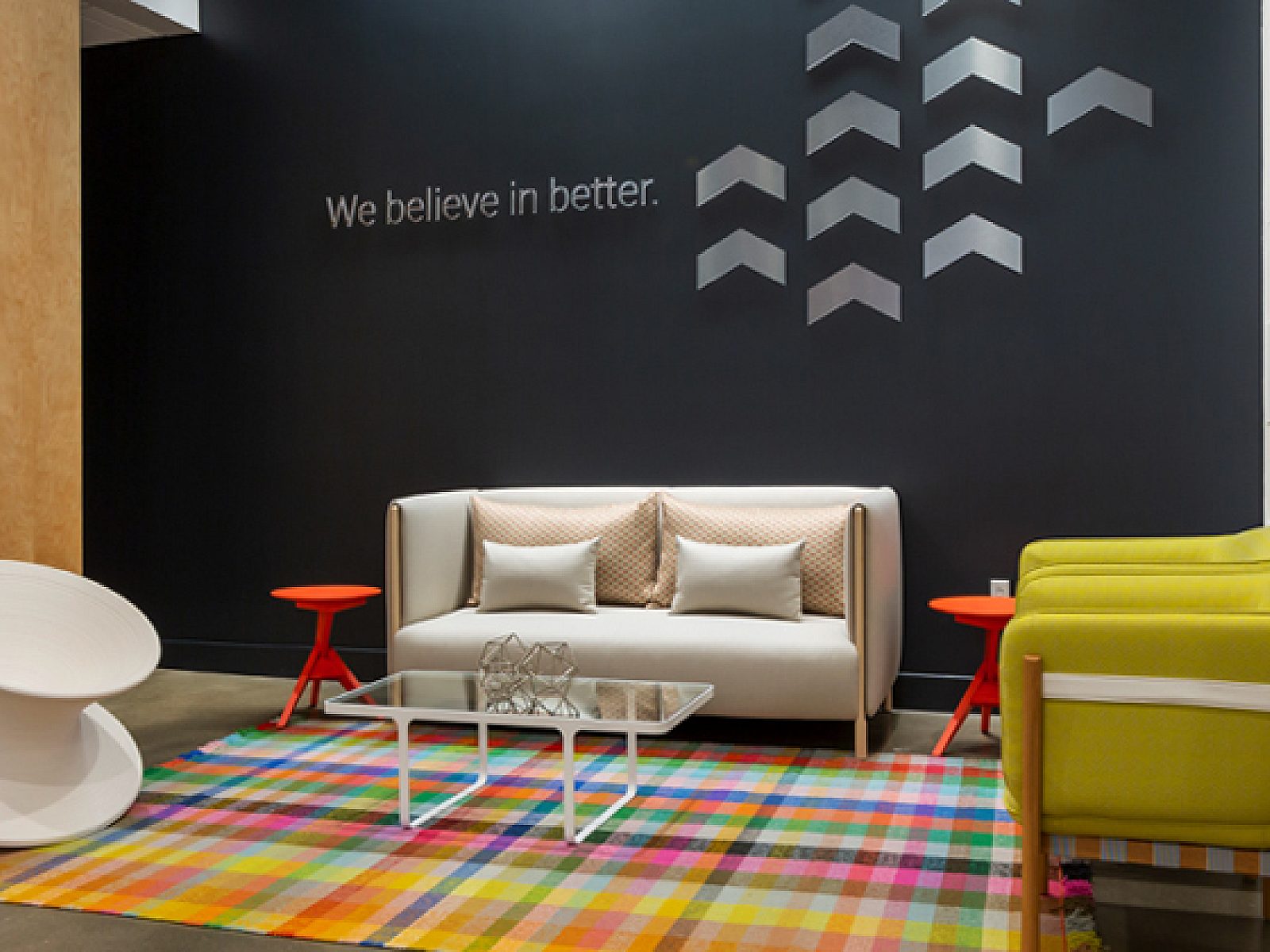 Clean, modern waiting area with colorful rug. Birch wall on left, dark wall in back & white tile wall on right. White sofa and lime green club chairs