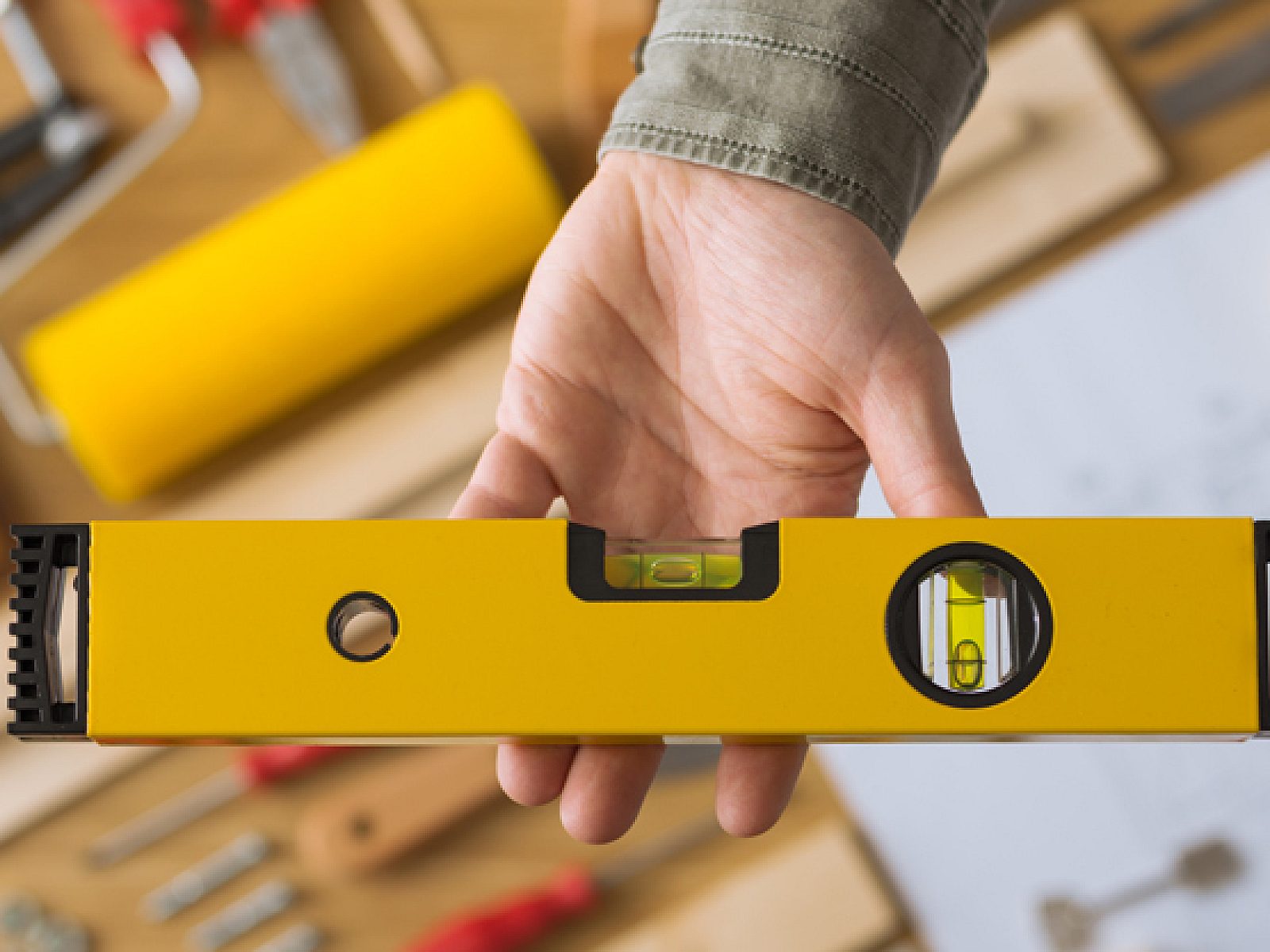 Flat-lay view of construction tools with hand holding a yellow bubble level