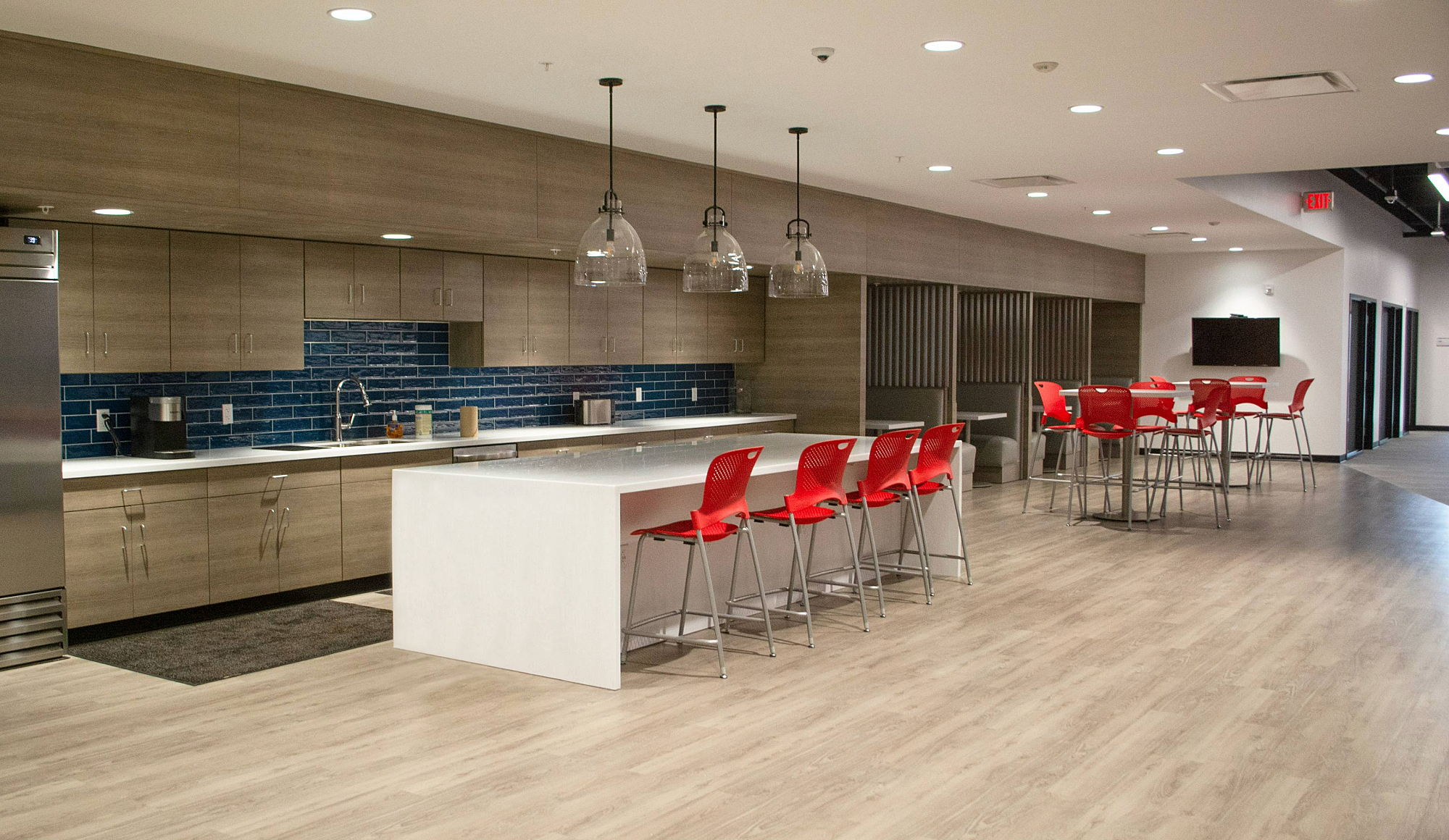 Bright, open kitchen & cafe with a white island, red chairs, and cozy booths along the far wall.