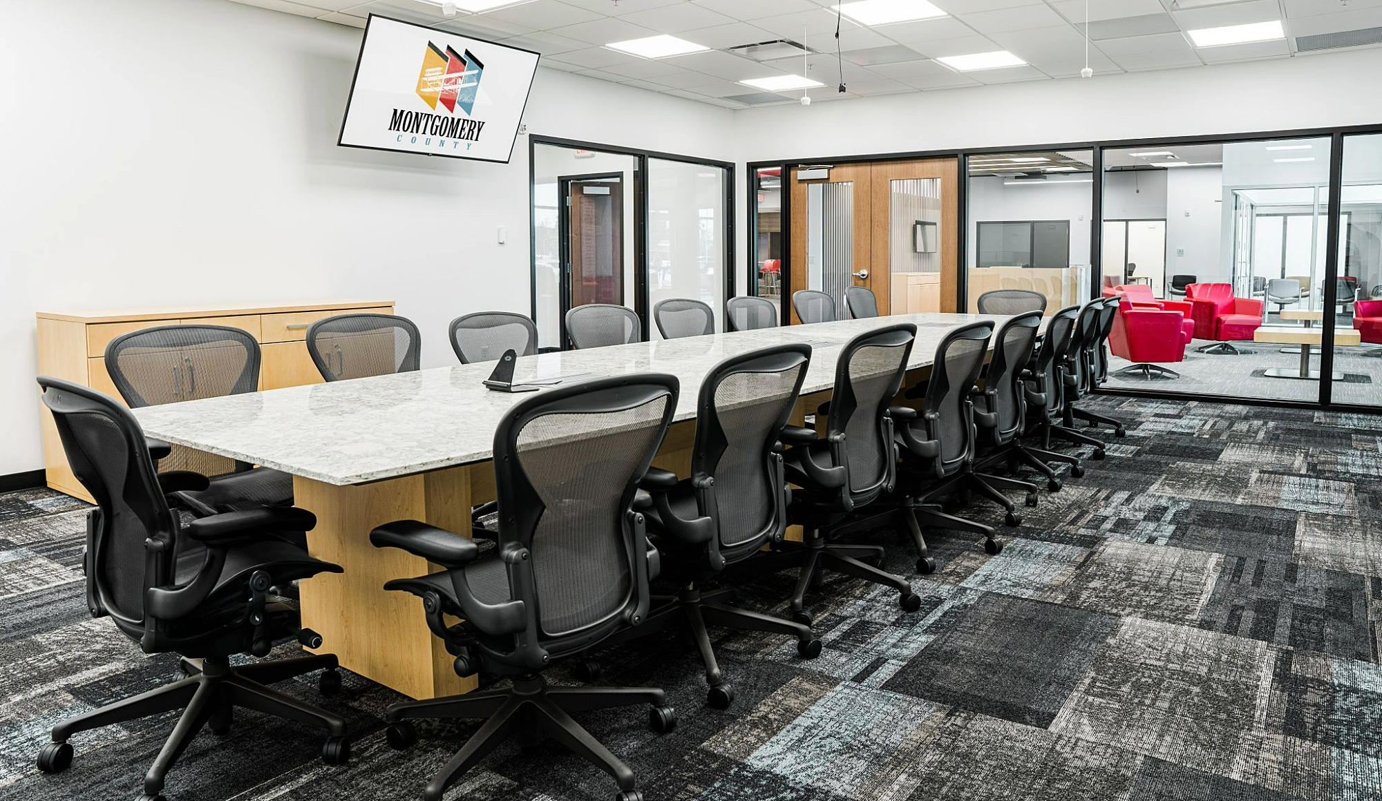Large conference room with comfortable mesh chairs, digital technology, and view of the lobby through floor-to-ceiling windows.