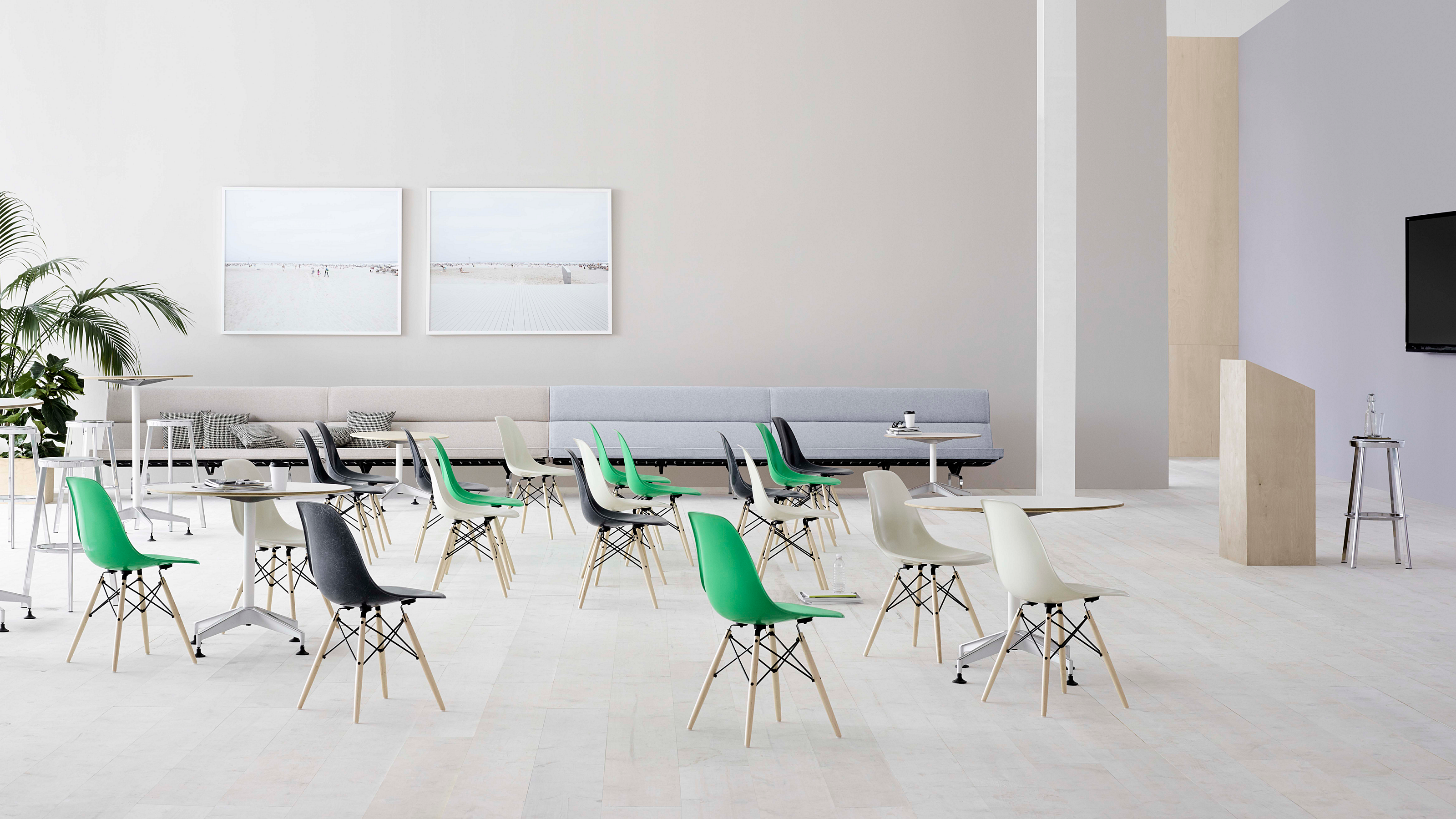 Large open room with round tables & chairs set for a conference. White walls & floor with a podium at right.