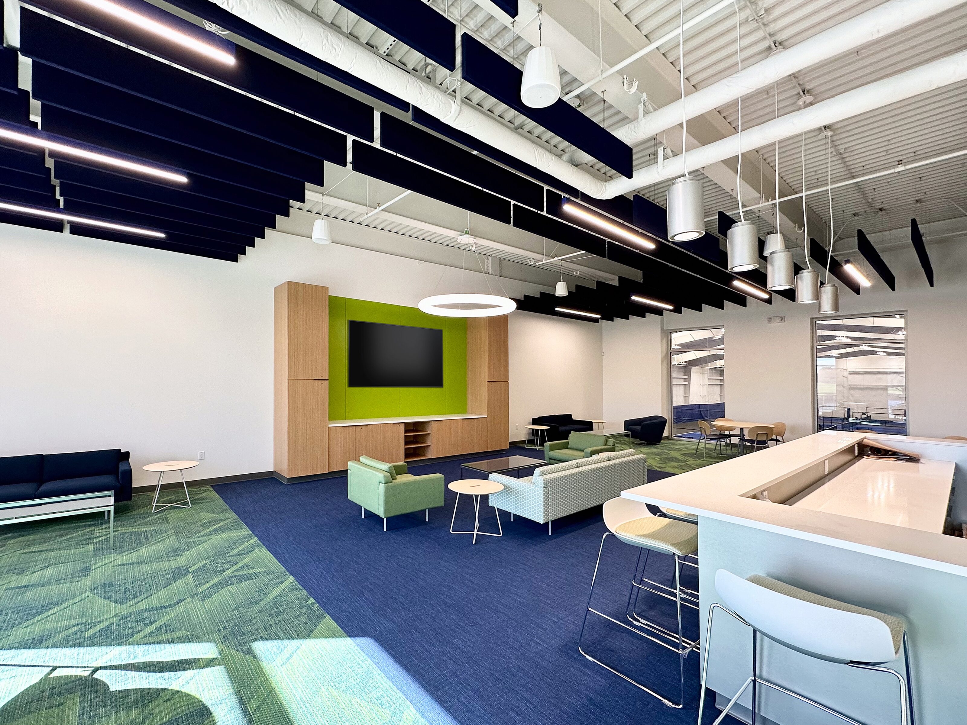 A spacious modern lounge with a mix of seating options, including sofas and chairs. To the right is a bar with sleek wire-base barstools.