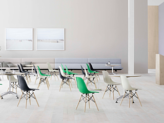 Large open room with round tables & chairs set for a conference. White walls & floor with a podium at right.