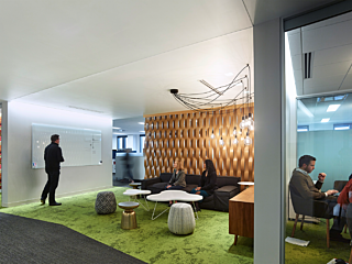Op-en-format gathering spacce within an office space. Partial view of people meeting in a glass-wall conference room.