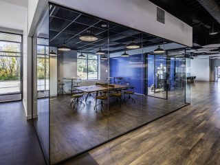 A stylish office with glass walls and warm wooden flooring creating a bright open workspace.