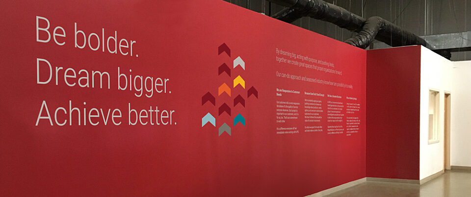 Red-painted wall in a tidy warehouse with inspirational brand message: Be bolder, dream bigger, achieve better.