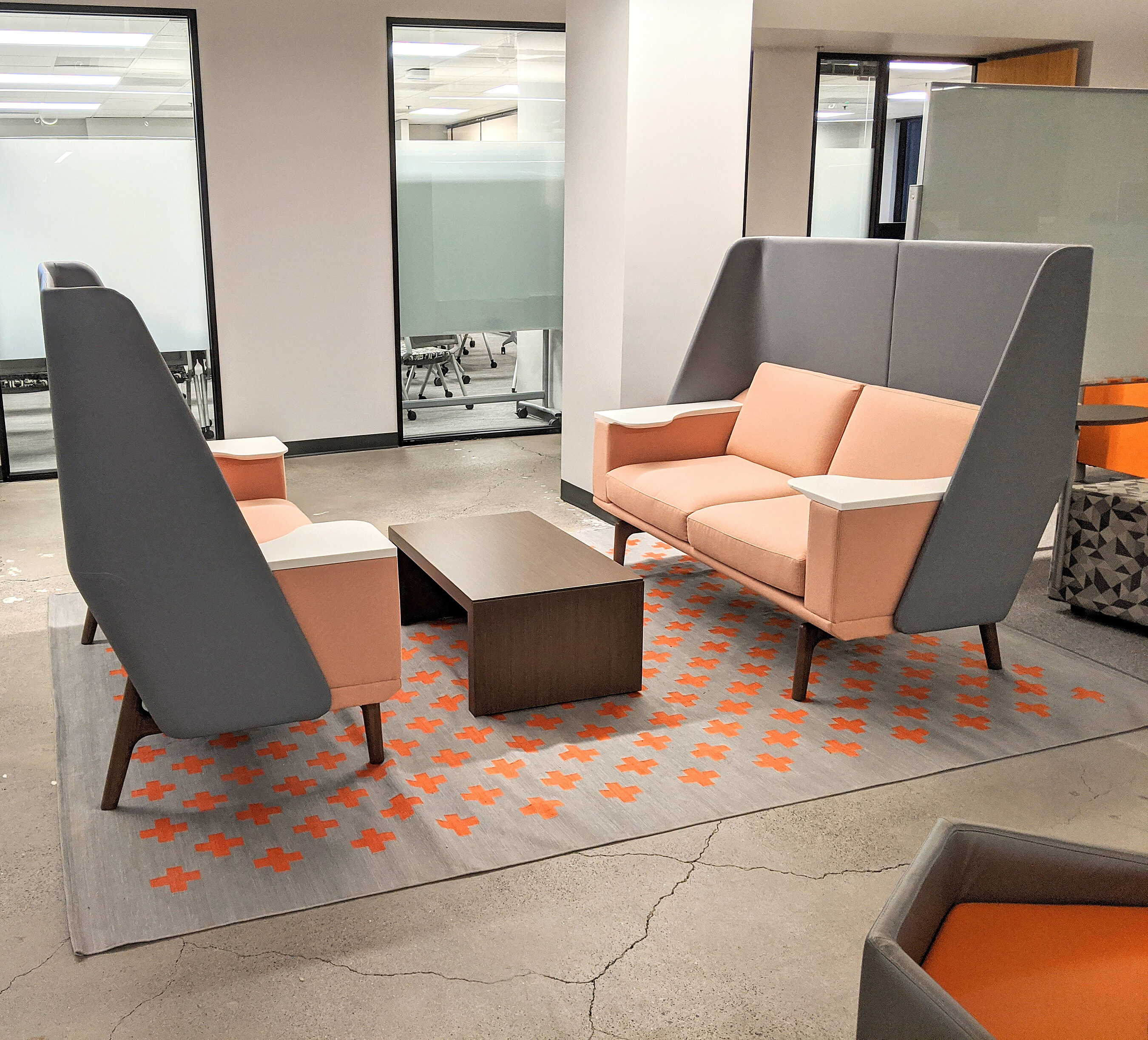 Polished concrete floor and mini sofas with tall backs for quiet work or meetings. Glass wall beyond with open meeting/conference space.