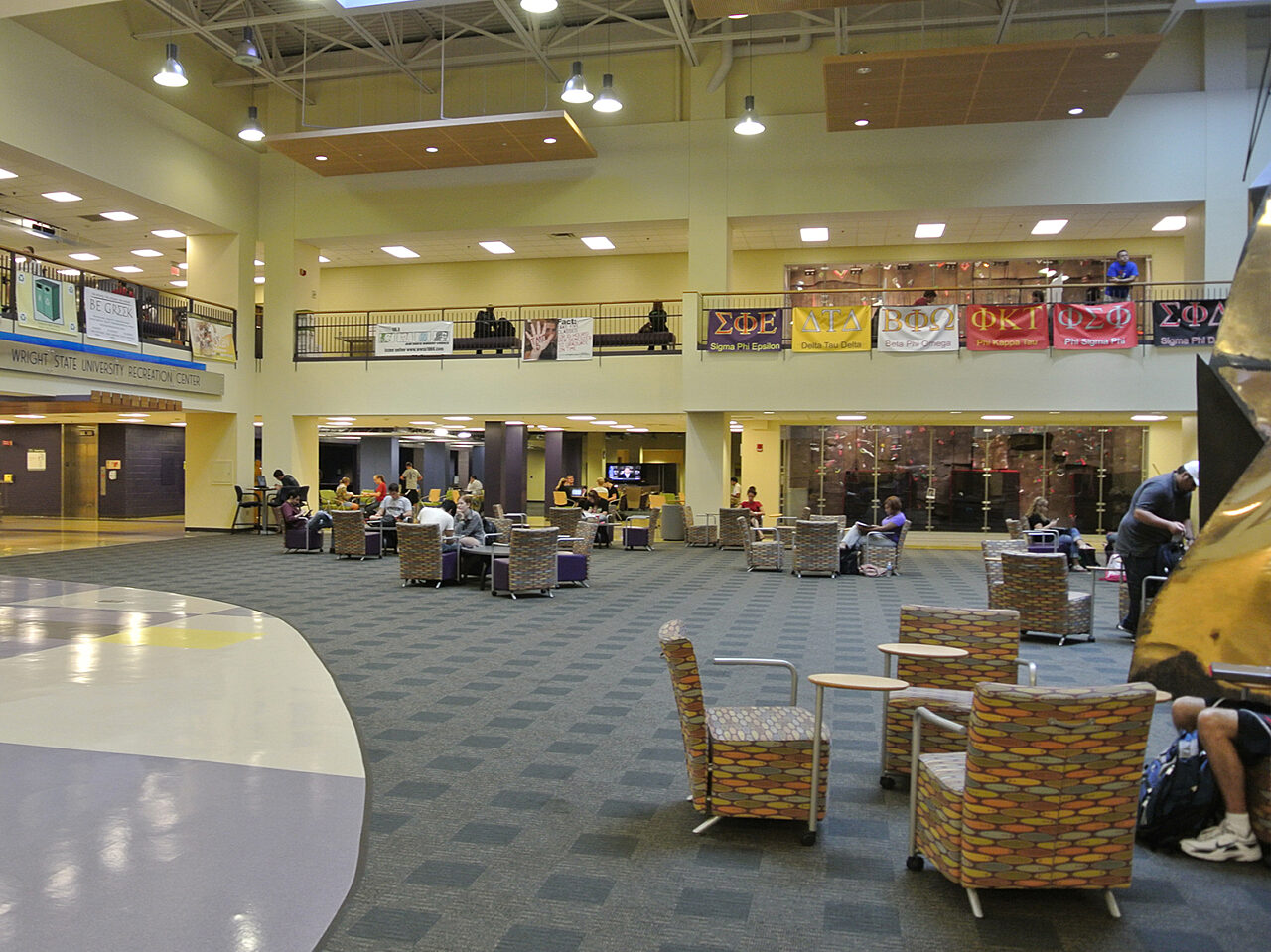 A spacious university center atrium featuring modern architecture and natural light, bustling with students and activity
