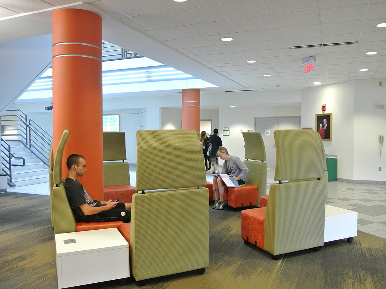 A group of individuals seated in large green and orange chairs within a spacious lobby area, engaged in conversation and relaxation.