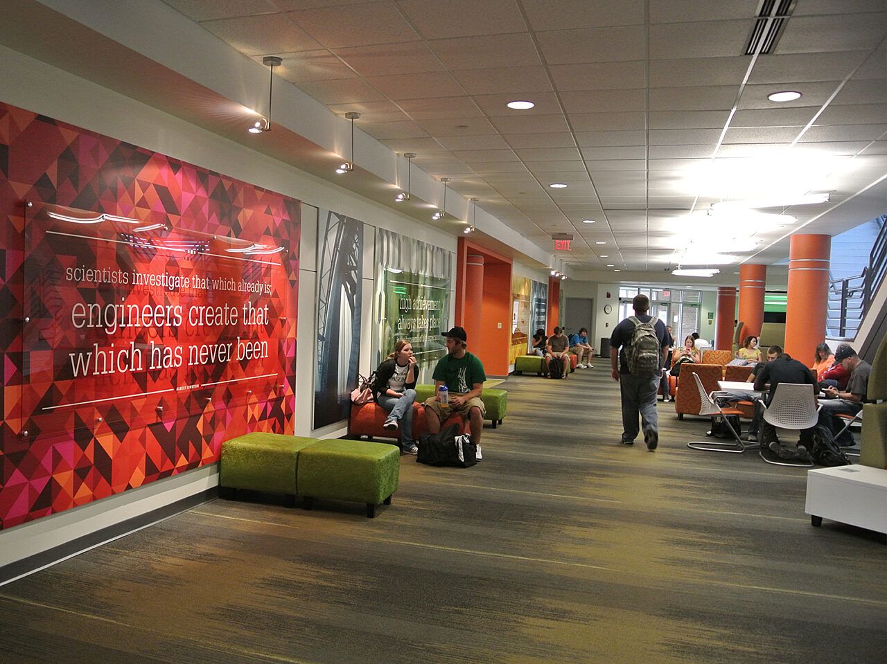 A group of individuals seated on vibrant green couches in a modern office environment, engaged in conversation.