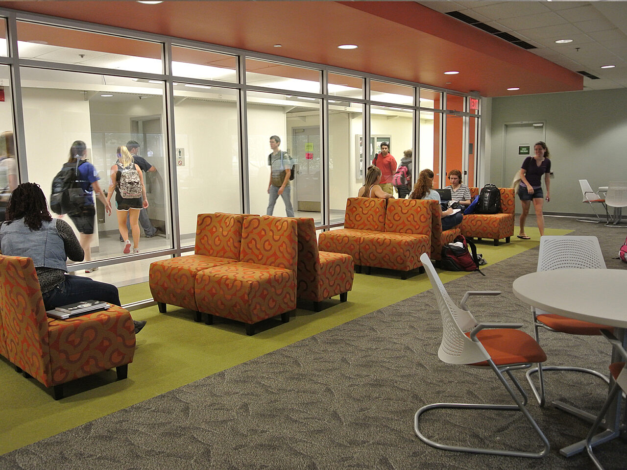 People gathered in a room, comfortably seated on bright orange chairs, engaged in conversation.