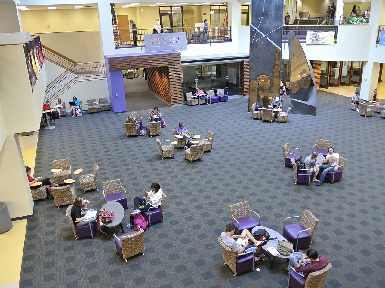 A spacious university center atrium featuring modern architecture and natural light, bustling with students and activity